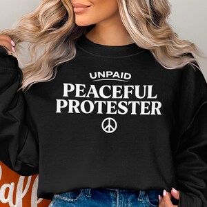 Black sweatshirt with "Unpaid Peaceful Protester" and a peace symbol.