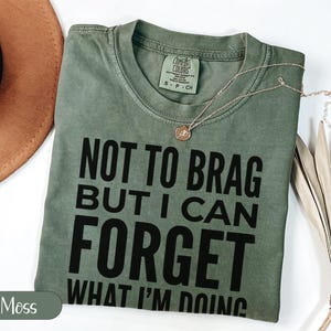 Green t-shirt with "NOT TO BRAG BUT I CAN FORGET WHAT I'M DOING" text.
