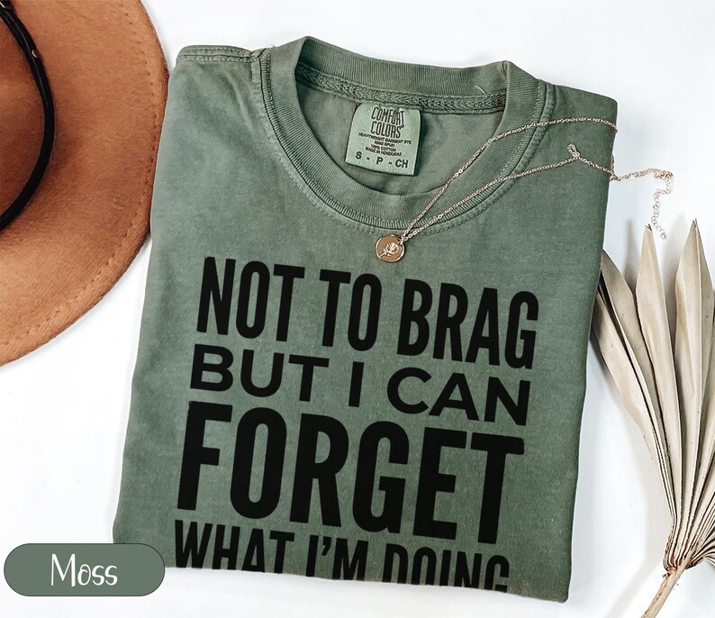 Green t-shirt with "NOT TO BRAG BUT I CAN FORGET WHAT I'M DOING" text.
