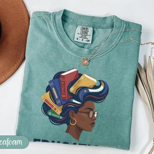 T-shirt with graphic of woman with books for hair, "Seafoam" text.