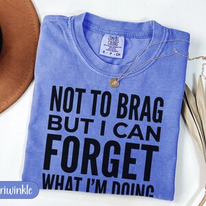 Periwinkle Comfort Colors t-shirt with "NOT TO BRAG BUT I CAN FORGET WHAT I'M DOING" text.