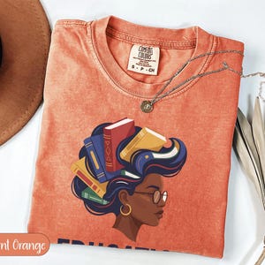 Orange t-shirt with graphic of woman with books for hair, Comfort Colors branding.