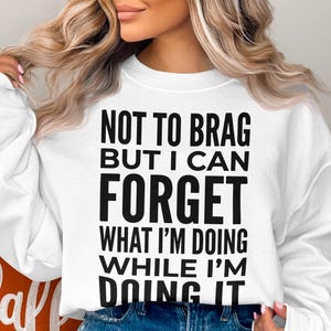 White sweatshirt with black text that reads "NOT TO BRAG BUT I CAN FORGET WHAT I'M DOING WHILE I'M DOING IT."