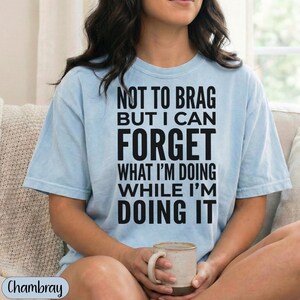 Light blue t-shirt with "NOT TO BRAG BUT I CAN FORGET WHAT I'M DOING WHILE I'M DOING IT" text.