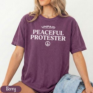 Berry colored t-shirt with "UNPAID PEACEFUL PROTESTER" and peace symbol.