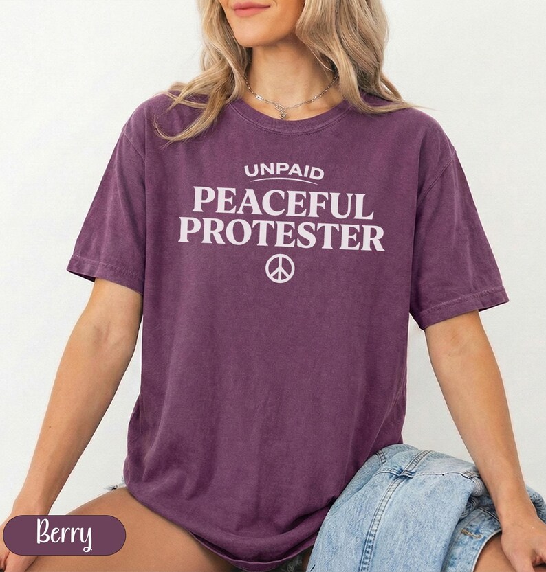Berry colored t-shirt with "UNPAID PEACEFUL PROTESTER" and peace symbol.