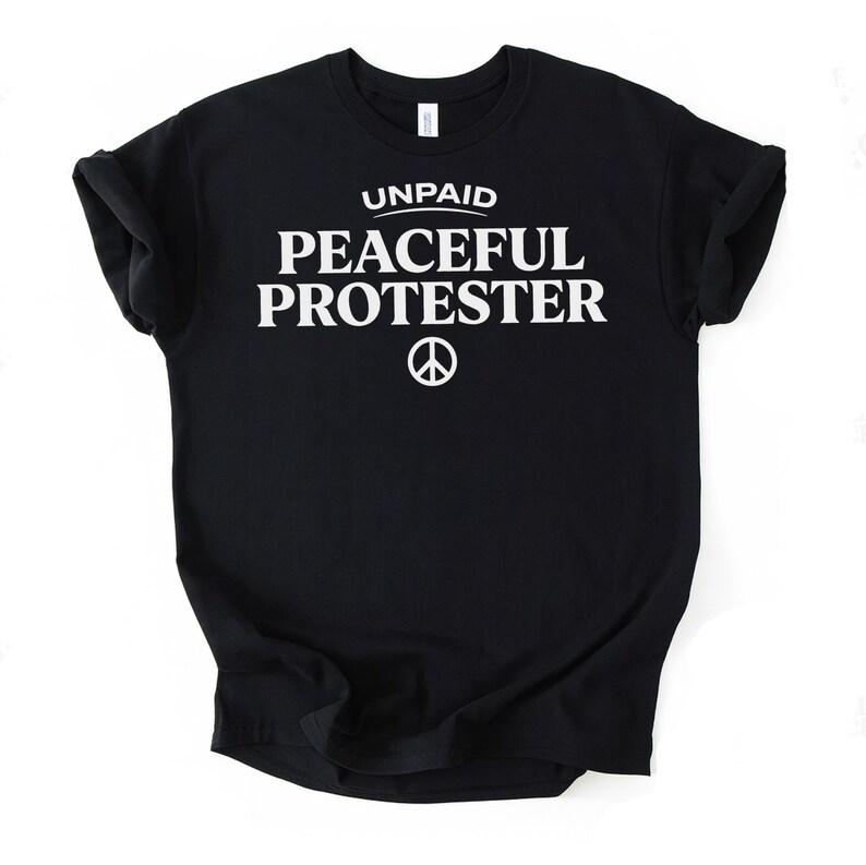 Black t-shirt with white text "UNPAID PEACEFUL PROTESTER" and peace symbol.