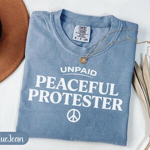 Blue t-shirt with "Unpaid Peaceful Protester" text and peace symbol.