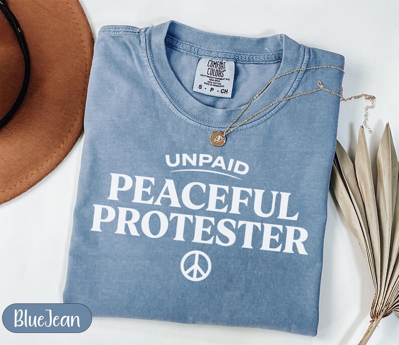 Blue t-shirt with "Unpaid Peaceful Protester" text and peace symbol.