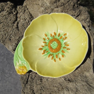 Puede incluir: Un plato de cerámica amarillo con forma de flor con hojas verdes y un centro marrón. El plato es perfecto para servir pequeños aperitivos o condimentos.