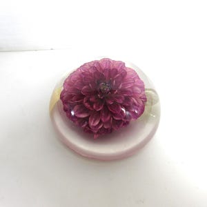 May include: A clear glass paperweight with a single pink flower inside. The flower is a dahlia with a yellow center.