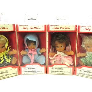 Può includere: Quattro bambole Baby Pee Wees vintage nelle loro scatole originali. Ogni bambola indossa un abito diverso e ha un'acconciatura unica. Le scatole sono rosse con la scritta "Baby Pee Wees" e un'avvertenza di pericolo di soffocamento.
