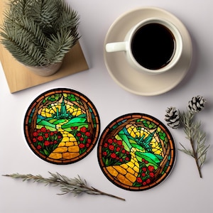 May include: Two round coasters with a stained-glass design featuring a yellow brick road, red flowers, and a green landscape. A cup of coffee and a small potted plant are also visible.