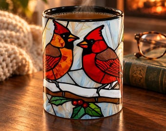 May include: A ceramic mug featuring a stained glass style design of two red cardinal birds perched on a snow-covered branch with green holly leaves and red berries. The mug has a black rim and contains a steaming hot beverage inside.