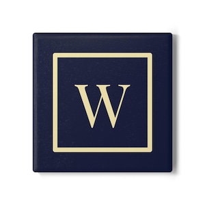 May include: A navy blue square coaster with a gold border and a gold letter "W" in the center. The coaster is a simple, elegant design, suitable for home decor.
