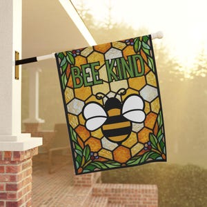 May include: A decorative outdoor flag featuring a stained-glass style design with a bee and the words "BEE KIND" in green. The flag has a honeycomb pattern in shades of yellow and orange, with green leaves and berries.
