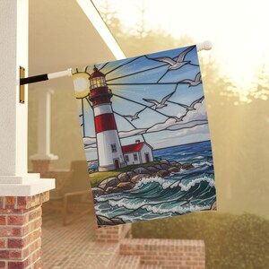 May include: A decorative outdoor flag featuring a lighthouse scene. The design includes a red and white striped lighthouse, a small white building, seagulls, and ocean waves. The artwork is set against a blue sky with a sun.