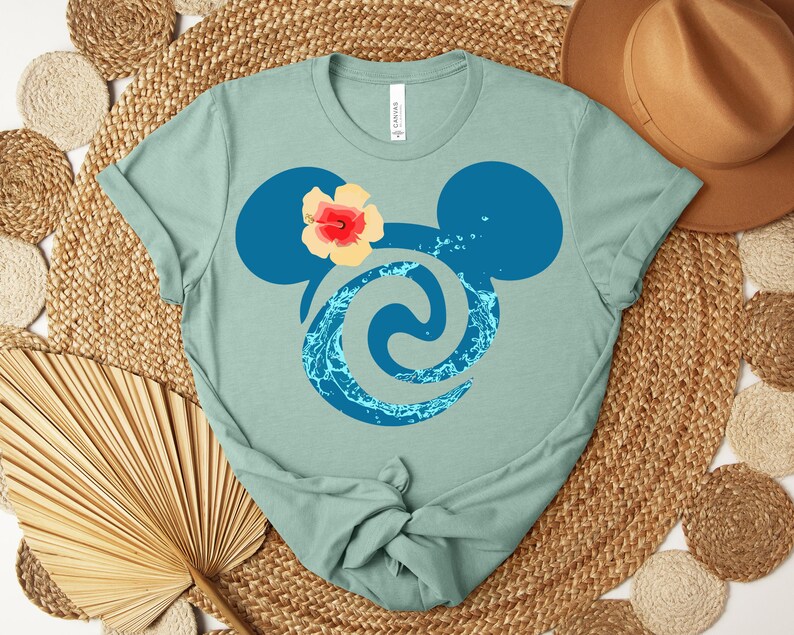Puede incluir: Camiseta de color verde azulado claro con un dise&ntilde;o de cabeza de Mickey Mouse azul, una flor de hibisco y un remolino acu&aacute;tico. La camiseta est&aacute; hecha de un material suave y es adecuada para uso casual.