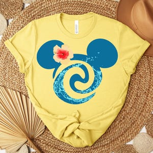 Puede incluir: Camiseta amarilla con una silueta azul de Mickey Mouse, un acento floral y un dise&ntilde;o acu&aacute;tico. La camiseta est&aacute; hecha de un material suave, ideal para el uso diario.