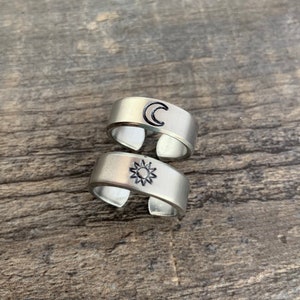 May include: Two silver rings with a sun and moon design. The rings are stacked on top of each other.