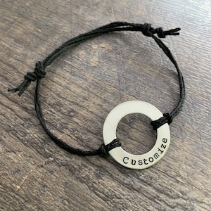 May include: A black cord bracelet with a silver ring charm that says "Customize" on it.