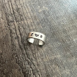 Op de afbeelding: Een zilveren ring met de letters "r ♥ a" gegraveerd.
