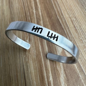 May include: A silver metal bracelet with the word "HI" engraved on it.