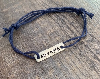 May include: A navy blue string bracelet with a silver charm that says "strength".