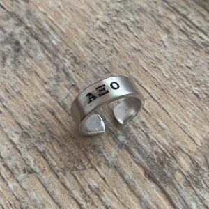 May include: A silver adjustable ring with the letters "AEO" engraved on it.
