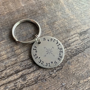 May include: Silver keychain with a compass and coordinates engraved on a round tag. The coordinates are 41° 53' 32.31" N 88° 28' 17.96" W.