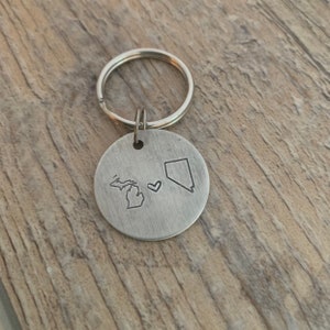 Può includere: Portachiavi in ​​argento con un cuore e i contorni del Michigan e del Nevada.