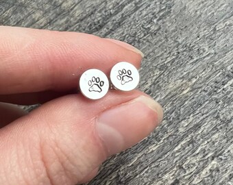 May include: A pair of silver stud earrings with a paw print design.