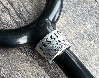 May include: A silver stethoscope charm with the name "JESSICA" engraved on it, surrounded by a design of small flowers and leaves.