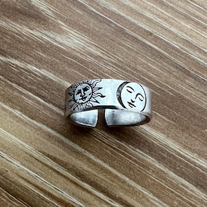 May include: A silver adjustable ring with a sun and moon design. The sun and moon have faces.