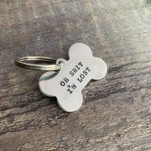 May include: Silver dog tag shaped like a bone with the text "Oh Shit I'm Lost" engraved on it.