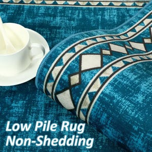 May include: A rolled-up teal low-pile rug with a geometric border design in white, black, and gray. The rug has a distressed texture and the text "Low Pile Rug Non-Shedding" is visible.