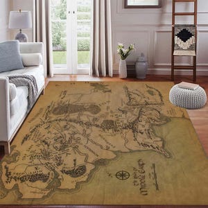 Puede incluir: Una alfombra rectangular grande con un mapa detallado de la Tierra Media en tonos marrones y beige. El mapa incluye características geográficas, etiquetas de texto y una rosa de los vientos. La alfombra está colocada sobre un suelo de madera.