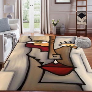 以下が含まれることがあります： 赤い唇、黄色い目、茶色とベージュの色調の顔が特徴の抽象芸術ラグ。 ラグはモダンなデザインで、リビングルームの木製の床に置かれています。