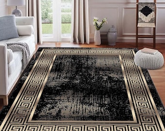 May include: A rectangular black area rug with a gold Greek key border. The rug has a distressed, textured appearance with a lighter beige center. The rug is placed on a hardwood floor in a living room setting.