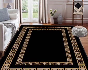 May include: A rectangular black area rug with a gold Greek key border design. The rug is placed on a hardwood floor in a living room setting. The rug's design adds a touch of elegance to the room's decor.