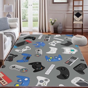 Puede incluir: Una alfombra rectangular gris con un patrón de mandos de videojuegos en negro, blanco, rojo y azul. Los mandos están dispersos por la superficie de la alfombra, creando un diseño lúdico y temático.