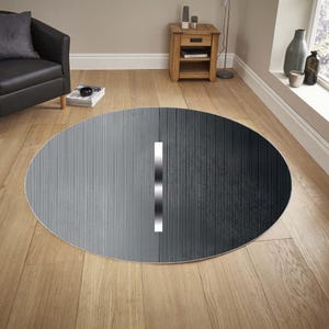 Pode incluir: Um tapete redondo com um design de metal escovado. O tapete apresenta um gradiente de cinza claro a cinza escuro, com uma faixa branca vertical no centro. Está colocado sobre um chão de madeira.