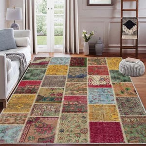 Op de afbeelding: Een rechthoekig patchwork vloerkleed met een verscheidenheid aan kleuren en patronen. Het vloerkleed heeft vierkanten in rood, geel, groen en blauw, met bloemen- en geometrische ontwerpen. Het vloerkleed ligt op een houten vloer in een woonkamer.