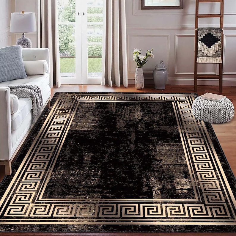 May include: A rectangular black area rug with a gold Greek key border. The rug has a distressed appearance with a dark, mottled pattern. The gold border frames the central design, adding a touch of elegance to the room.