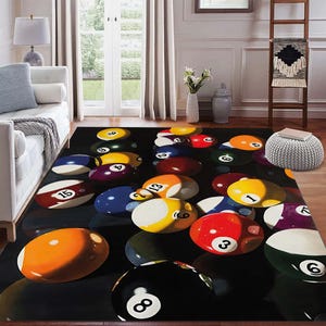 May include: A rectangular area rug featuring a realistic depiction of scattered billiard balls on a black surface. The balls are in various colors, including yellow, red, blue, and orange, with white numbers. The rug adds a playful touch to any room.