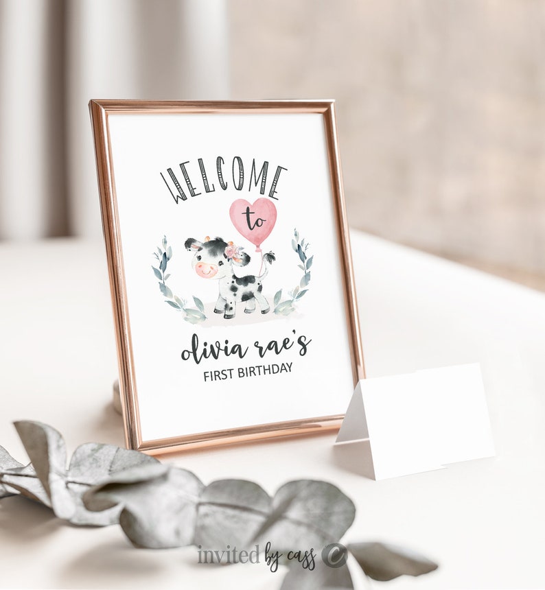 May include: A printable welcome sign for a first birthday party. The sign features a black and white cow with a pink balloon and the text "Welcome to Olivia Rae's First Birthday".