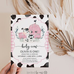 May include: A pink and white cow with black spots stands in front of a pink barn with a black rooster on top. The text "holy cow" is written in black script. The text "Olivia is one!" is written in black. The text "Please help us celebrate" is written in black. The text "Saturday | June 20th | 2-4pm" is written in black. The text "at the sandhill residence" is written in black. The text "1234 hilltop way, herring tn" is written in black. The text "rsvp to cass @ 999.999.9999" is written in black. The text "invited by cass" is written in black. The text "C" is written in black.