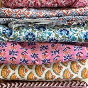 Puede incluir: Una pila de telas plegadas con diversos diseños florales y geométricos en tonos rosa, azul, amarillo y burdeos. Las telas, probablemente de algodón, son adecuadas para proyectos de patchwork o artesanía. Medidas no disponibles.