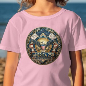 Pink t-shirt with circular patriotic emblem featuring eagle, stars, and "America 250".