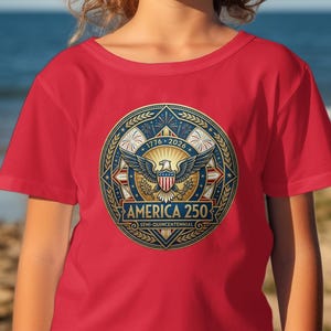 Red t-shirt with circular "America 250" emblem featuring eagle and fireworks.